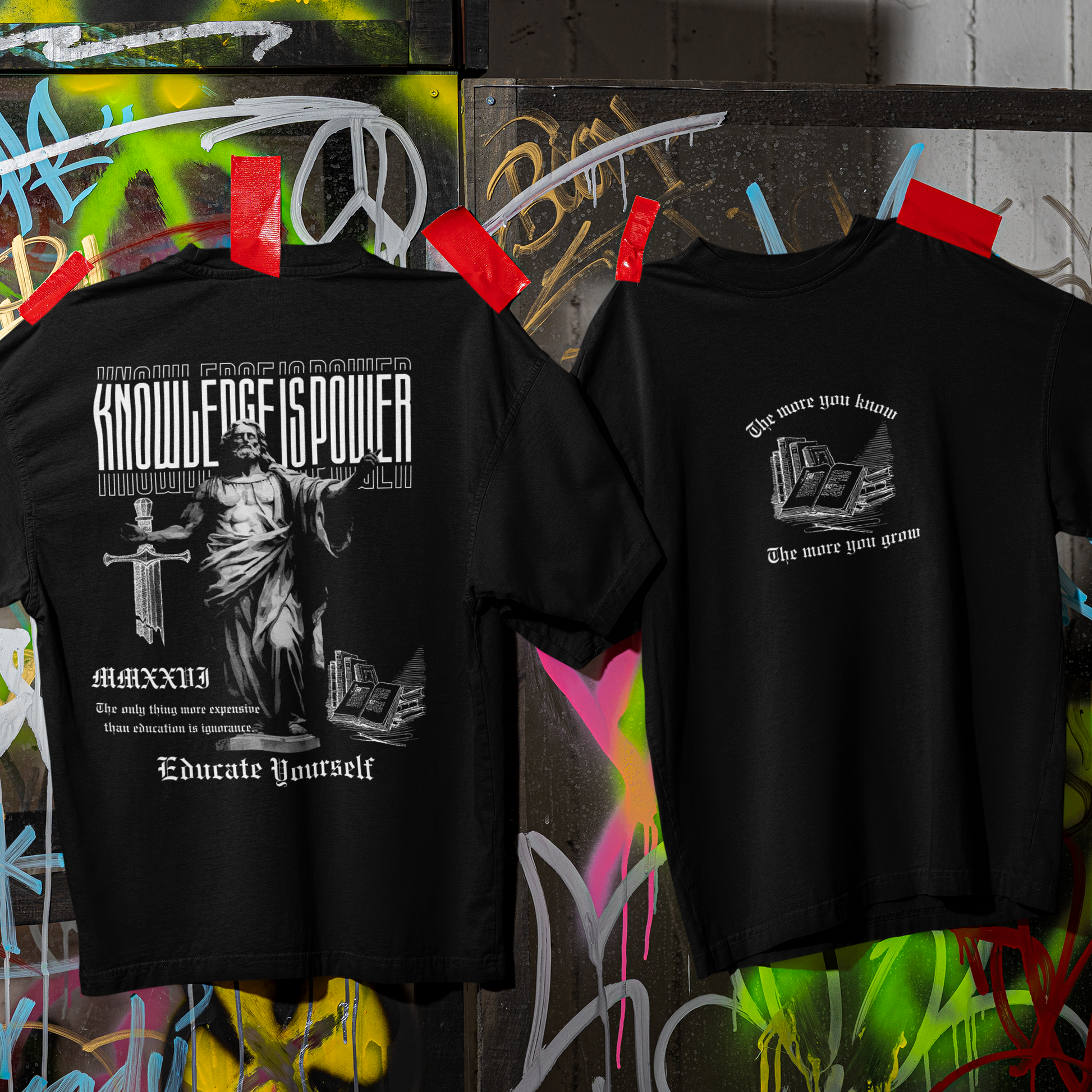 Two black t-shirts with graphic designs on a graffiti-covered wall background